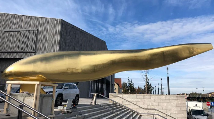 Abstract golden sculpture resembling a long, smooth shape near stairs