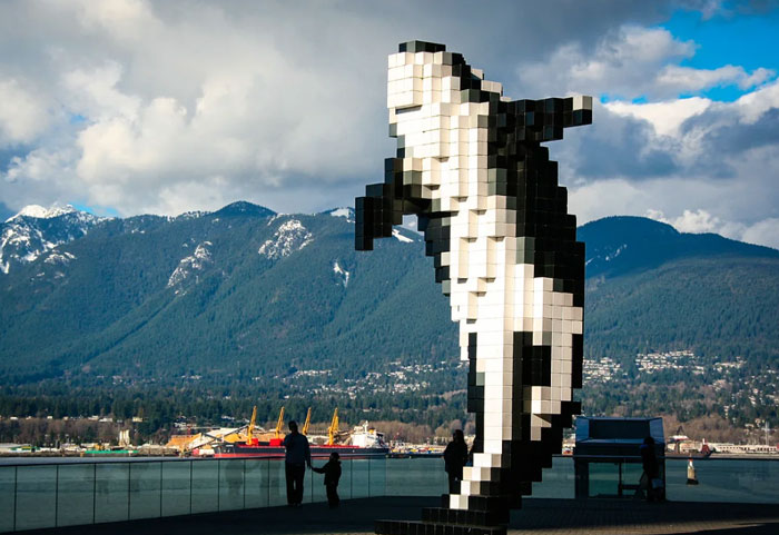 Pixelated orca whale statue with mountains and harbor in background