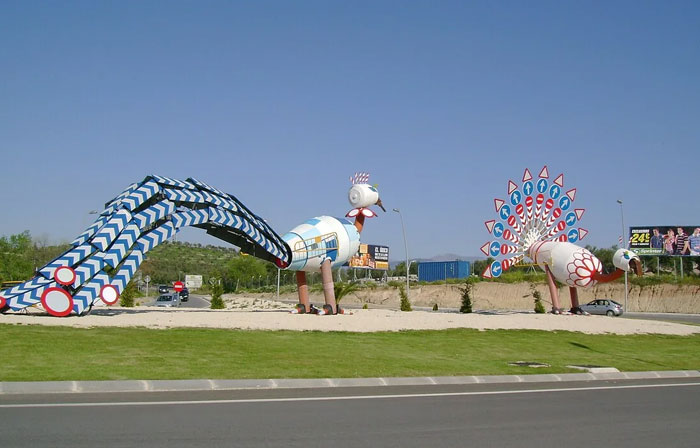 Ugly monument of two stylized peacocks with patterned tails by the roadside