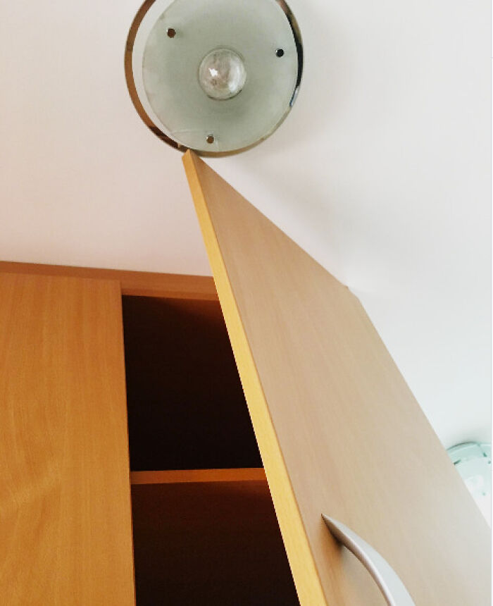 An open cabinet door hitting a ceiling light fixture, an evident architecture and design fail in kitchen planning.