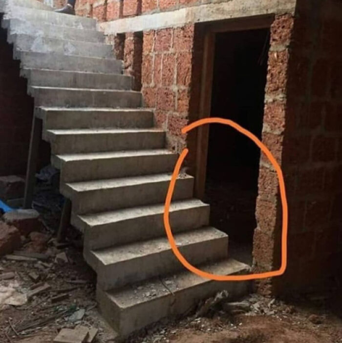 An architectural design fail: a doorway awkwardly placed beneath a concrete staircase, rendering it unusable.