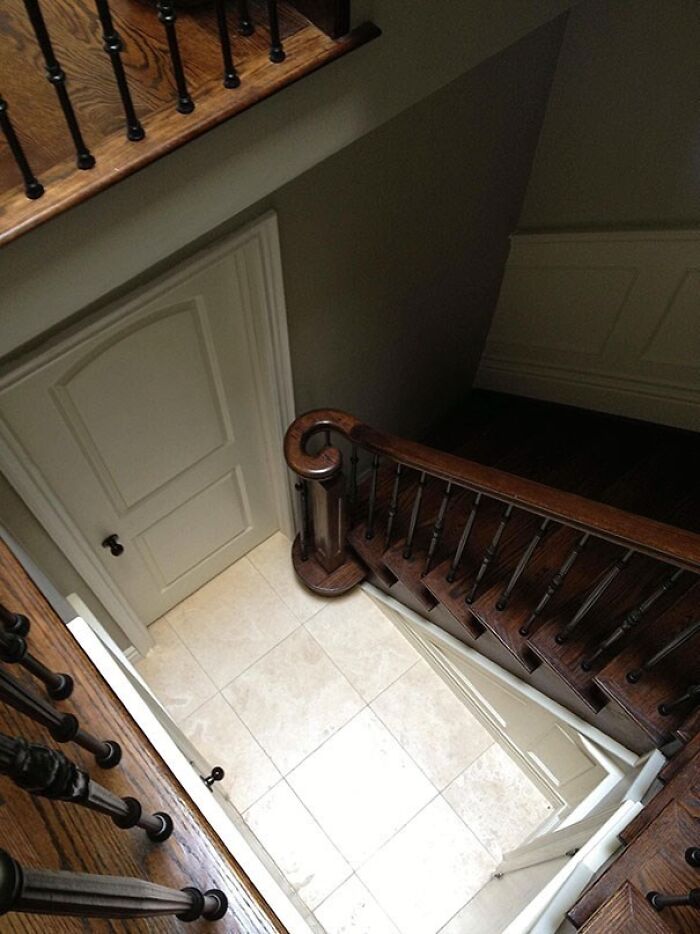 A door at the bottom of a dark wooden staircase, illustrating an architecture and design fail.