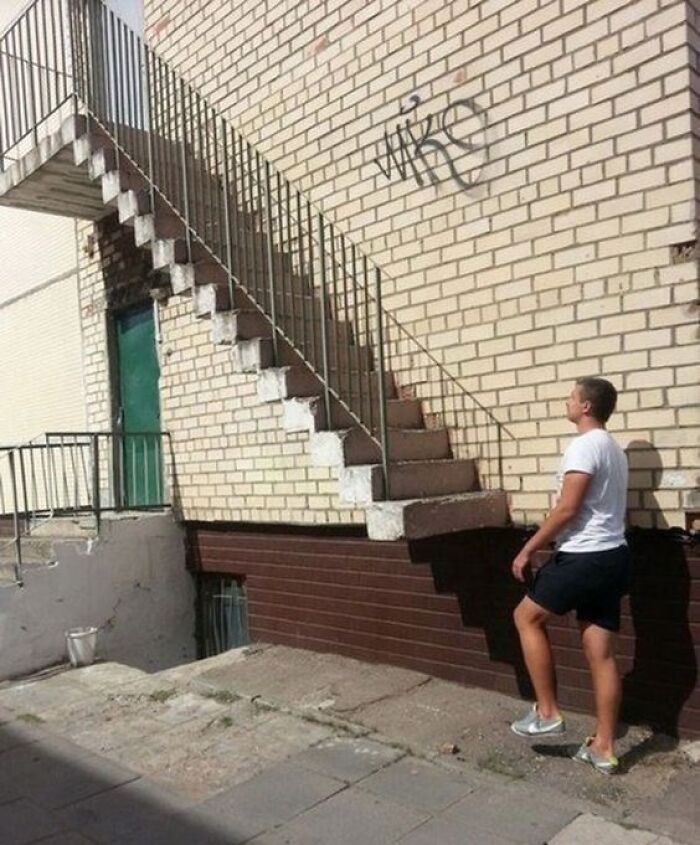 A man looking up at an external staircase leading to a brick wall, an architecture and design fail.