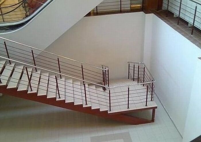 An indoor staircase with metal railings leads to a wall, an evident architecture and design fail.
