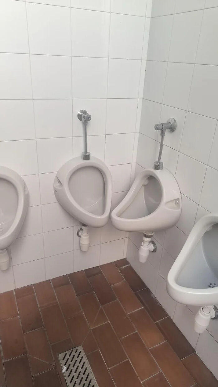 Three urinals in a public restroom; two are positioned extremely close together in a corner, showcasing an architecture design fail.