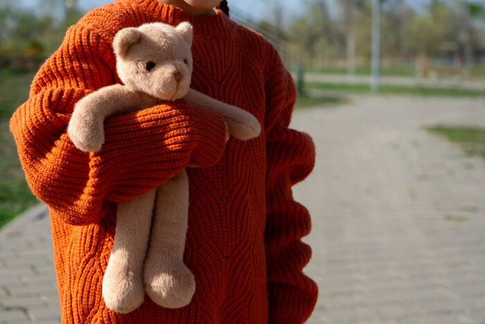 Child in orange sweater holding teddy bear representing lost innocence in breakups