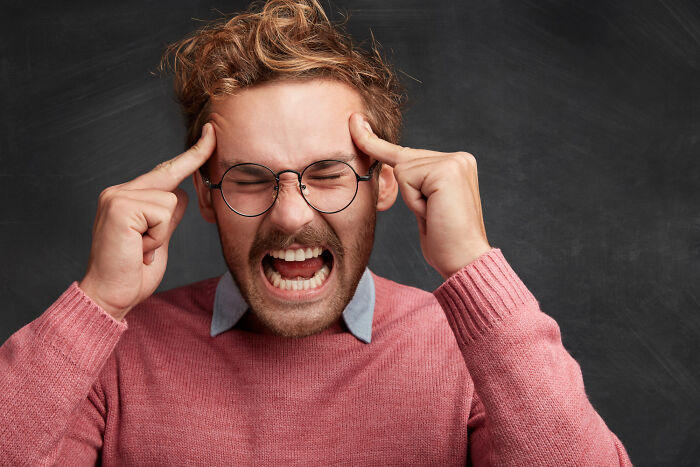 Frustrated man with glasses screaming and holding head in pain