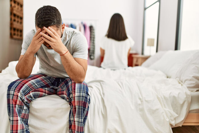 Stressed man sitting on bed with woman turned away in bedroom