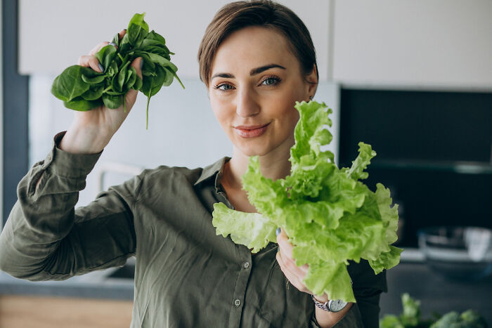 Smiling woman holding fresh lettuce and spinach indoors