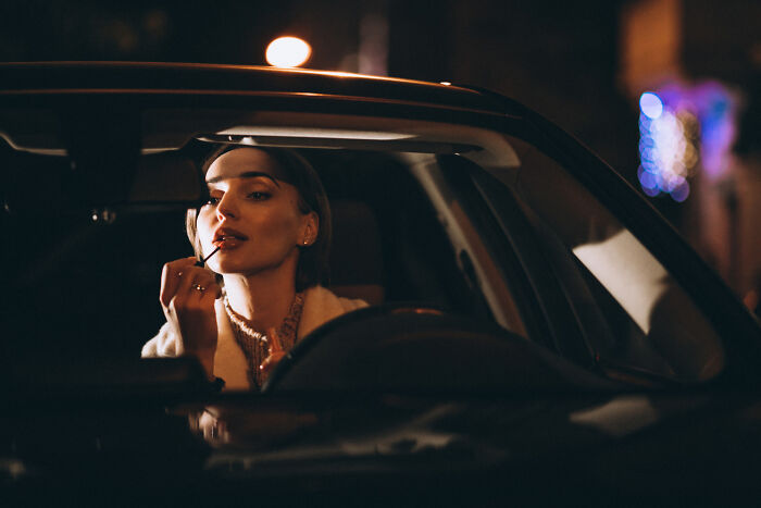 Woman applying lipstick in car at night, depicting relationships that derailed and breakup stories