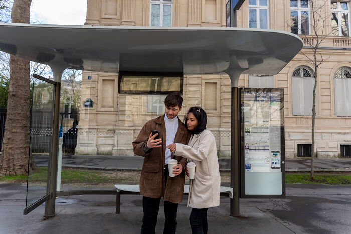 Young couple checking phone together at bus stop