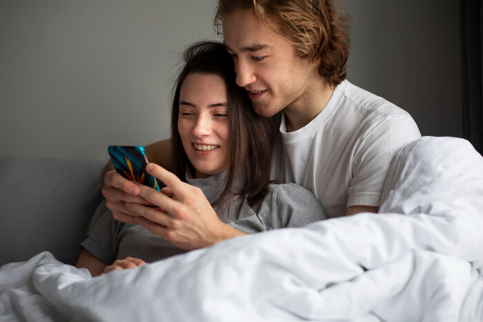 Couple smiling together while looking at phone in bed