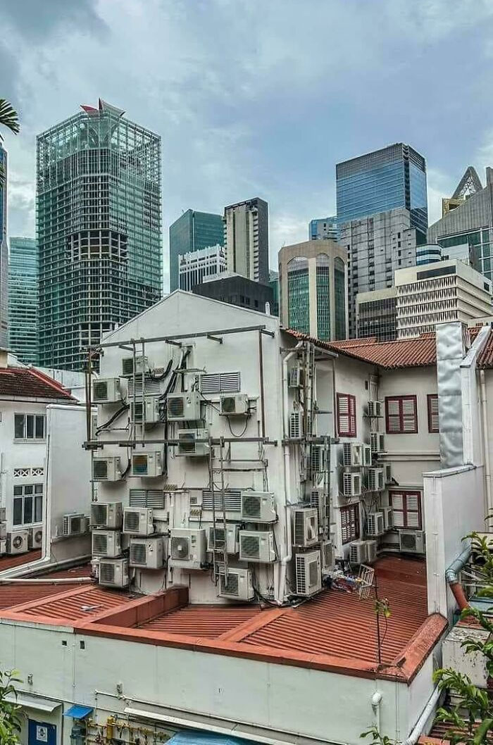 Urban building cluttered with numerous air conditioners and city skyscrapers in the background