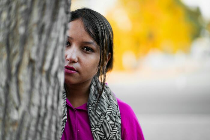 A woman peeking from behind a tree with a serious expression, symbolizing hidden double lives.