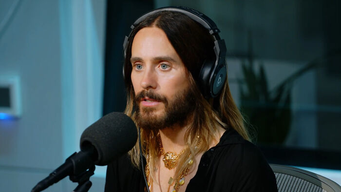 Jared Leto, a celebrity, with long hair and headphones, recording a podcast, whose fame continues.