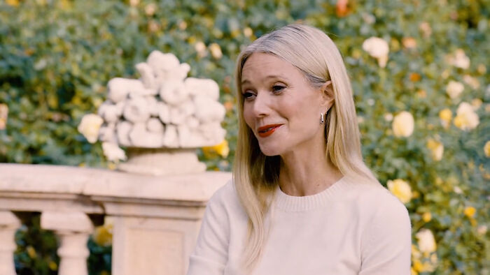 Blonde female celebrity with red lipstick and white sweater, smiling with a background of yellow flowers, whose fame ran out.