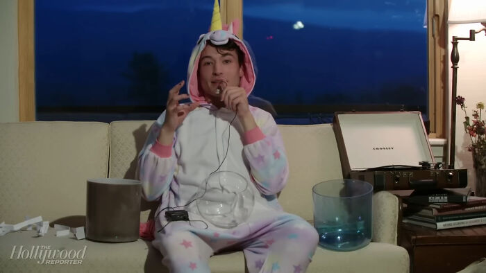 A man in a unicorn onesie talking into a microphone, representing celebrity scandals.