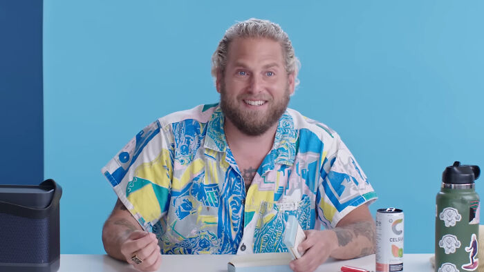 Bearded male celebrity in a colorful shirt, smiling at a table with a drink can and water bottle, whose fame ran out.