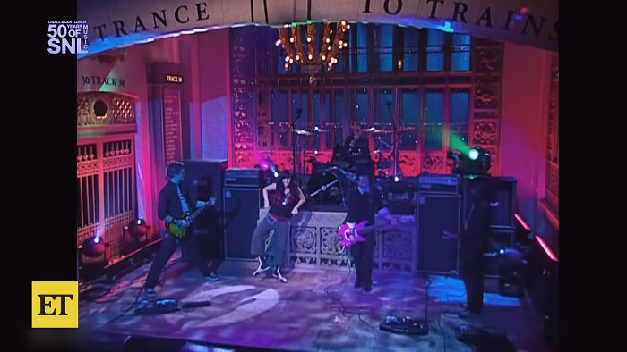 A band performs on stage with purple and blue lighting, part of celebrity scandals.