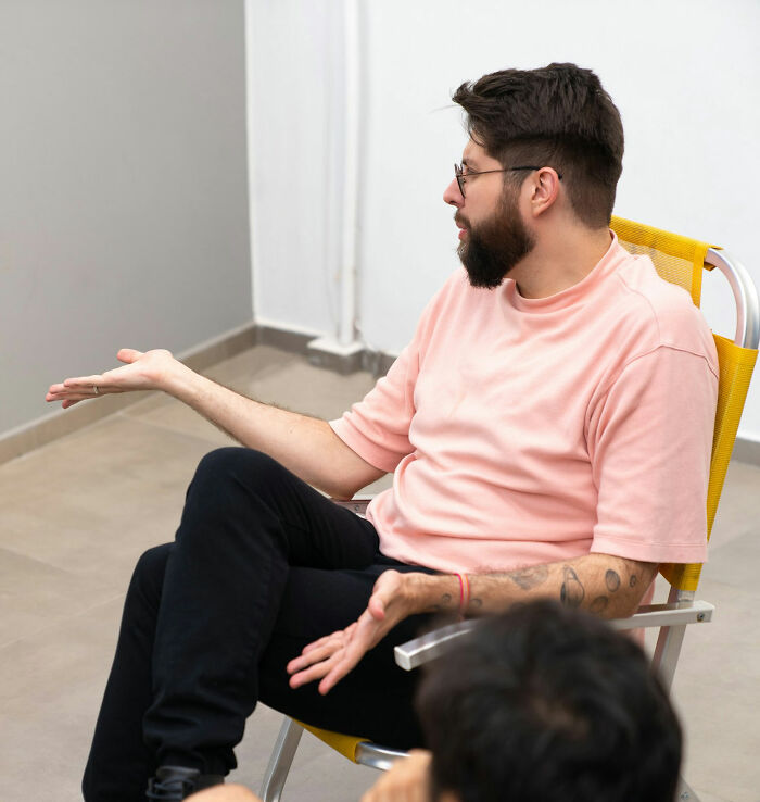 A man with a beard and glasses sitting and gesturing, showing hints that a person is secretly very smart.