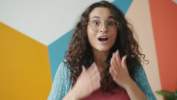 Excited woman with glasses in colorful room expressing surprise