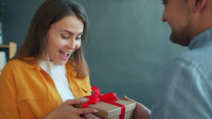A woman is happily surprised receiving a gift from her partner, a moment that could make her decide to marry her partner.