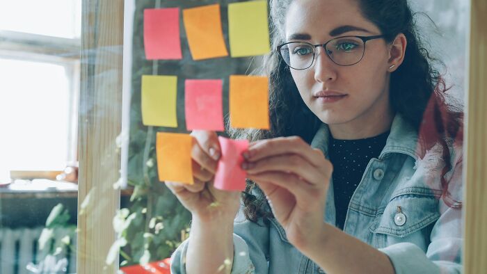Woman focusing intensely placing sticky notes on glass board to organize thoughts, related to anxiety patterns