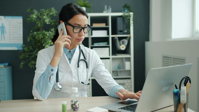 A female doctor on a call, working on her laptop in an office. A silly solution that works.