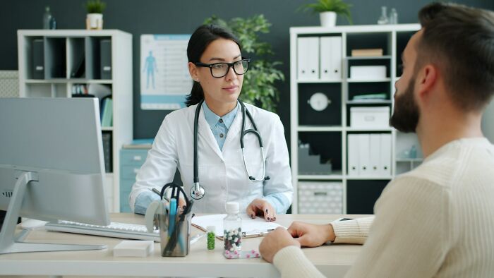 A female doctor discusses intense stress and burnout with a male patient in a modern clinic office.