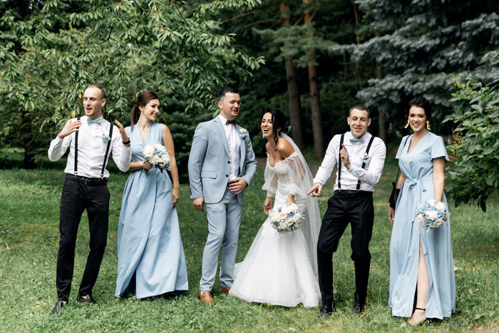Bride, groom, and bridal party in blue and grey posing outdoors at a wedding Bride, groom, and bridal party in blue and grey posing outdoors at a wedding