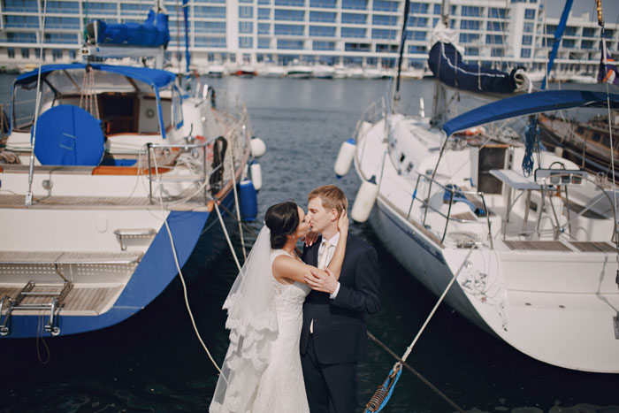 Bride and groom kissing between docked boats during wedding photoshoot by the marina Bride and groom kissing between docked boats during wedding photoshoot by the marina