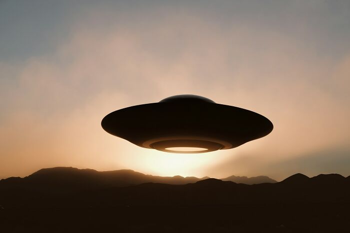 A flying saucer hovers over mountains at sunset, an unexplainable experience or encounter.