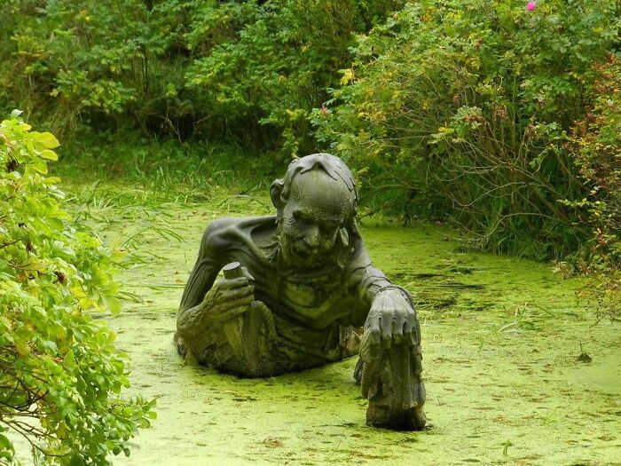Terrifying mossy statue of man emerging from swamp water in eerie forest scene