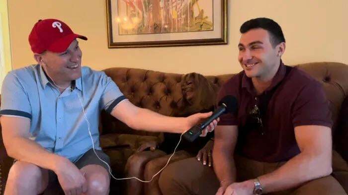 Man interviewing a smiling friend at home holding a microphone with recorder