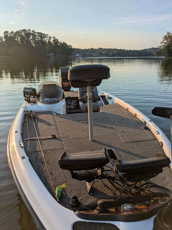 Empty fishing boat docked on calm lake at sunset with fishing rods and electronics