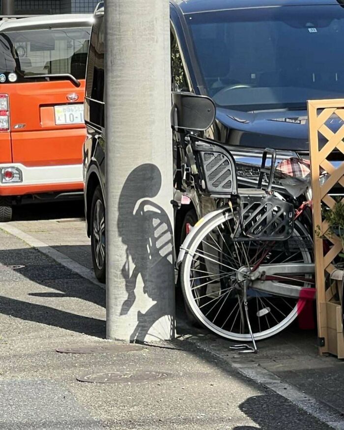 Shadow on pole creates alien figure with bicycle details in parking area