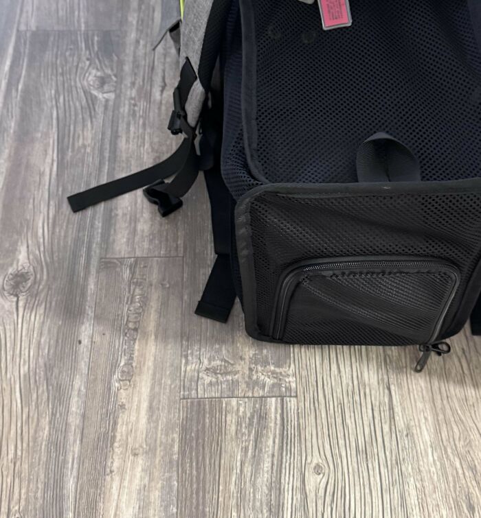 Black mesh backpack on wood floor with visible straps and zipper