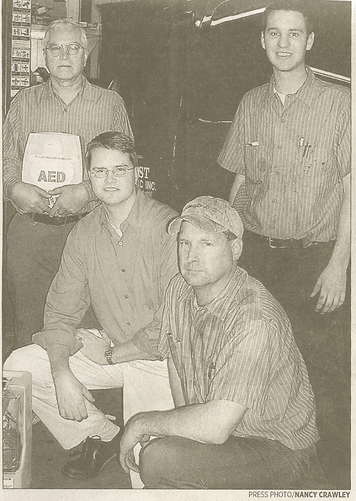 Group of four men posing in work shirts with industrial equipment in background