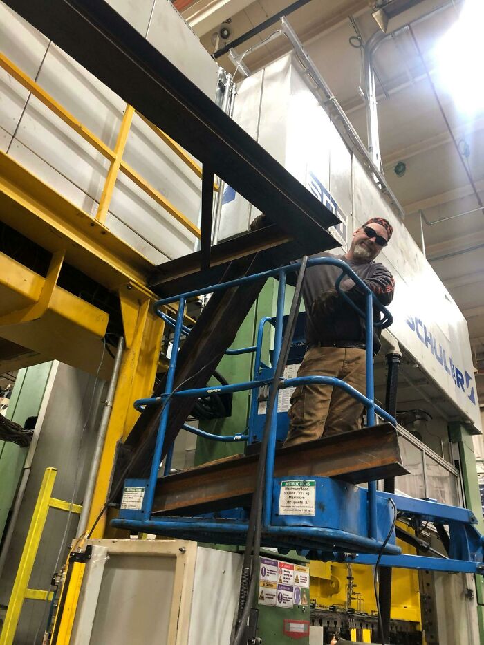 Man working on blue lift near heavy industrial machine in factory setting with steel beams
