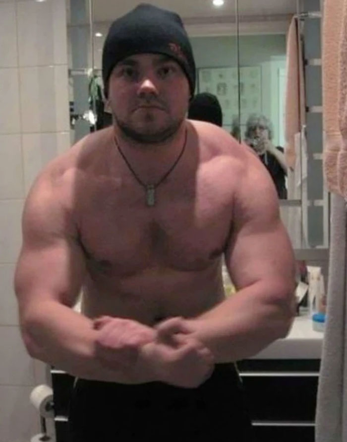 A muscular man in a beanie flexing in a bathroom with a ghostly reflection, creating a When You See It picture.