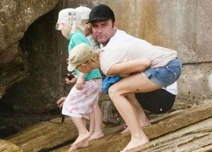 A man with two children, appearing to have a woman's legs in a confusing when you see it picture.