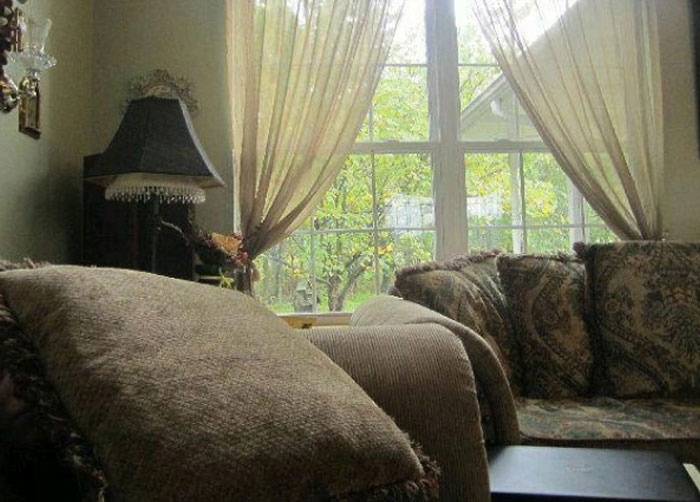 A living room with a large window and curtains, a When You See It picture.
