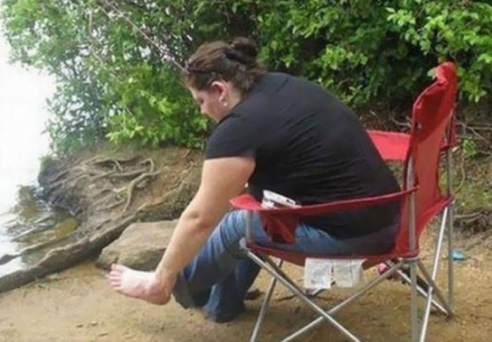 Woman sitting in a red chair by the water, appearing to have a very long foot. A funny 'When You See It' picture.