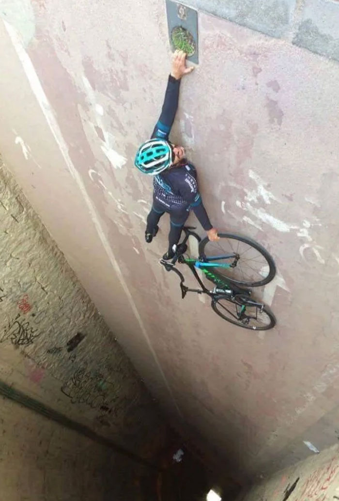 A cyclist holding a bicycle, standing on a steep concrete incline. When You See It, the perspective makes the wall look like a floor.