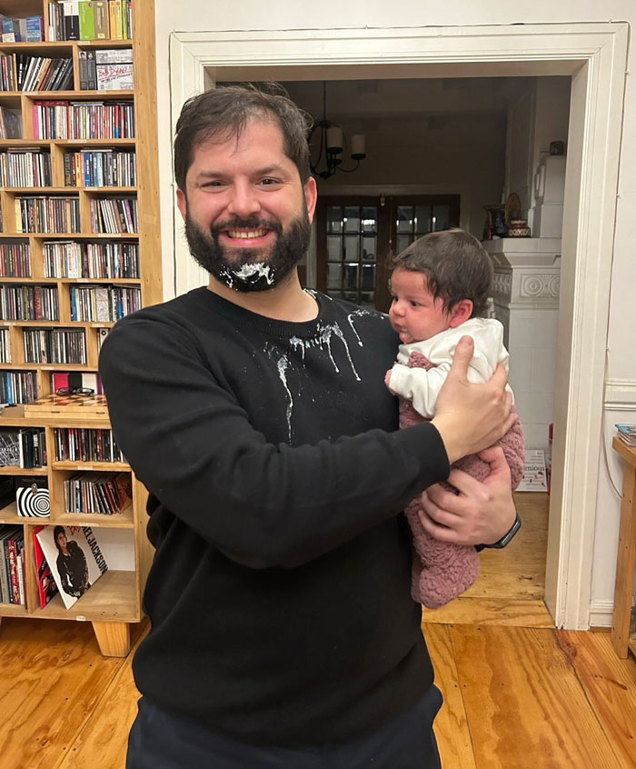 Smiling world leader holding a baby with food on his face indoors