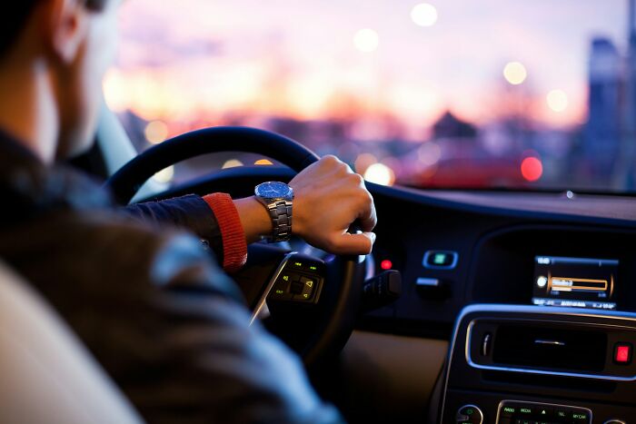 A person driving a car at dusk, seen from behind the shoulder, showcasing a silly solution that works.