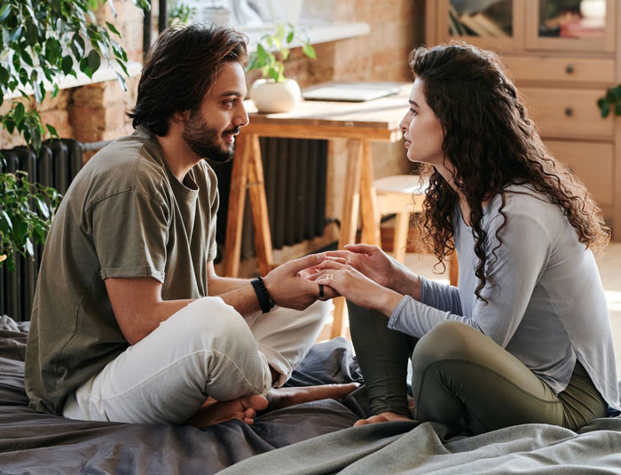 A pregnant woman and her husband sit facing each other on a bed, holding hands, discussing their divorce. A pregnant woman and her husband sit facing each other on a bed, holding hands, discussing their divorce.
