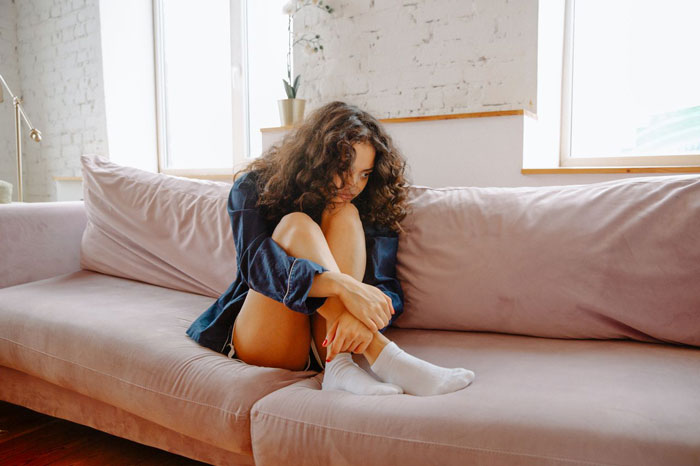 Pregnant woman on a couch looking distraught, contemplating divorce from husband who grieves his late ex. Pregnant woman on a couch looking distraught, contemplating divorce from husband who grieves his late ex.