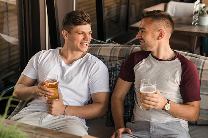 Two men happily drinking beer and chatting on a couch Two men happily drinking beer and chatting on a couch