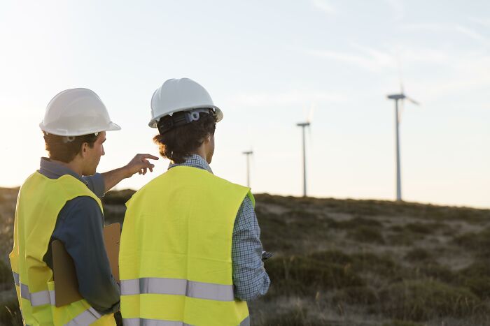 Two engineers in hard hats observing wind turbines, showcasing careers safe from AI job displacement.